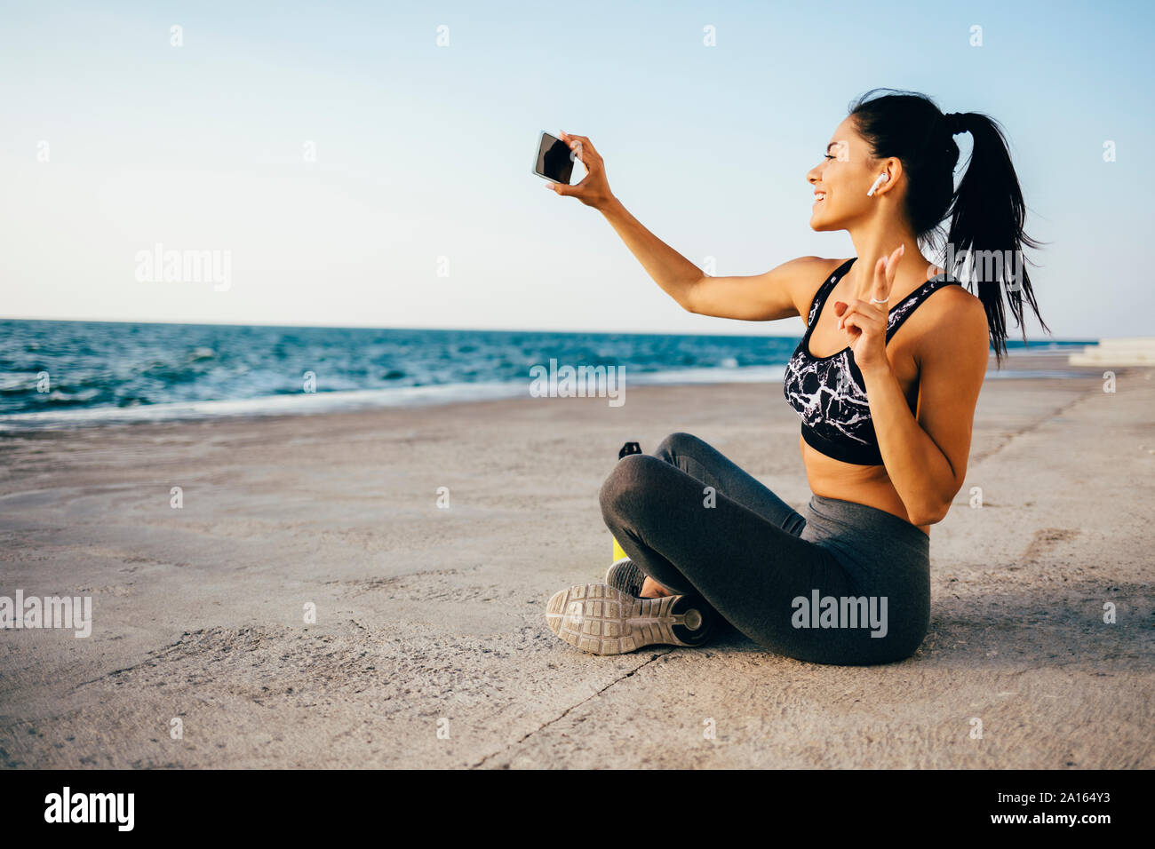 Woman using smartphone and taking a selfie, sitting on a pier Stock Photo
