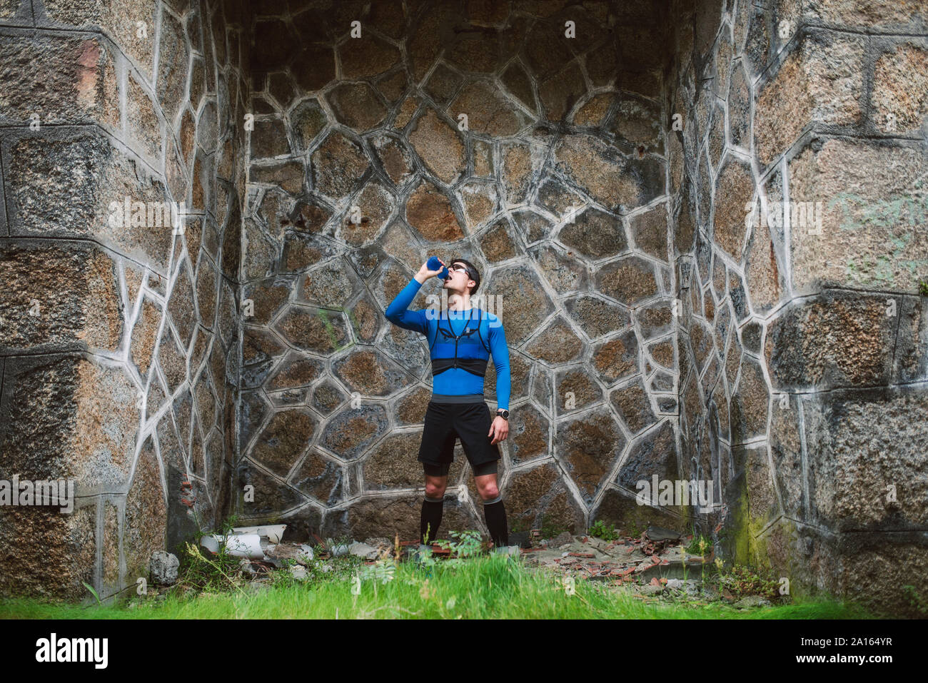 Trail runner standing at a wall drinking water Stock Photo