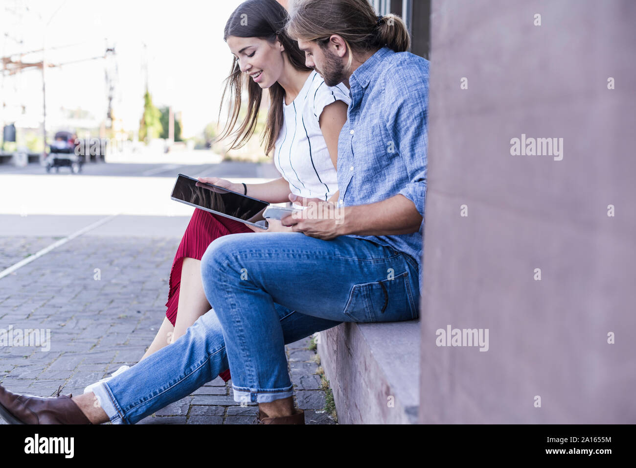 Young couple sitting on windowsill at a building using a tablet Stock Photo
