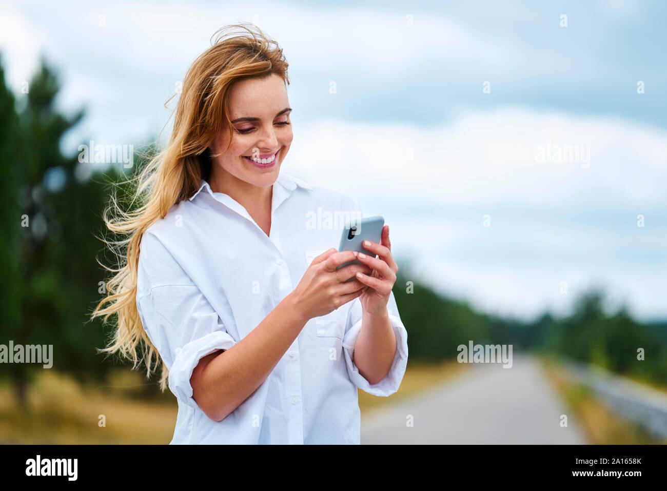 Happy woman checking cell phone on rural road Stock Photo