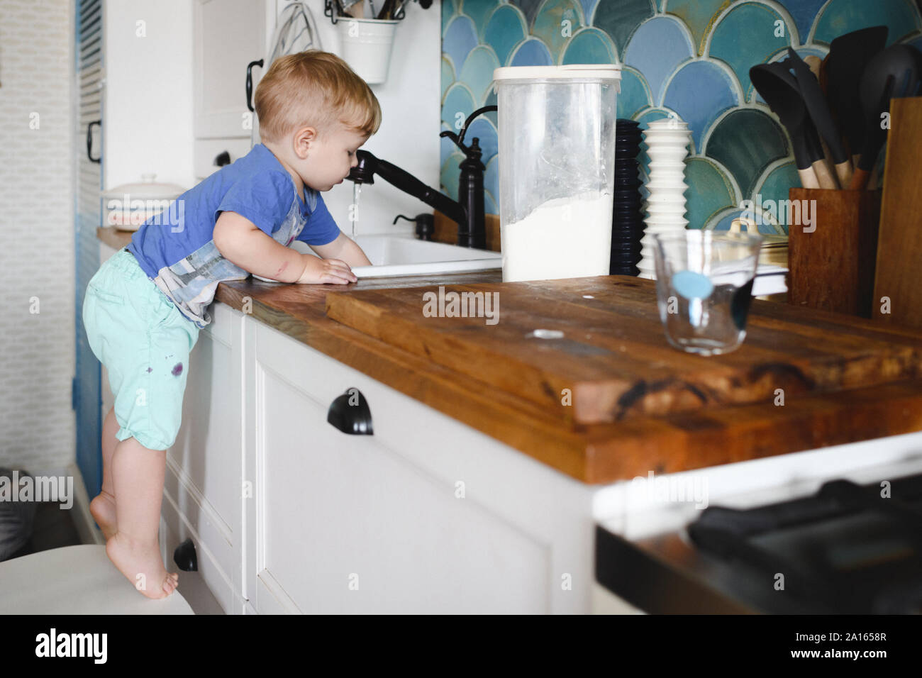 Little boy standing on tiptoes on chair in kitchen washing dishes Stock Photo