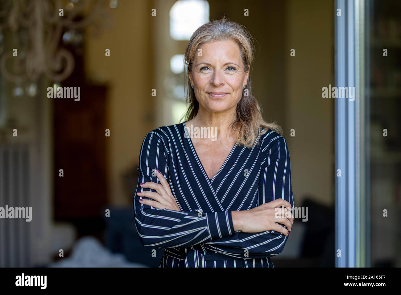 Portrait of smiling mature woman standing at opened terrace door Stock Photo