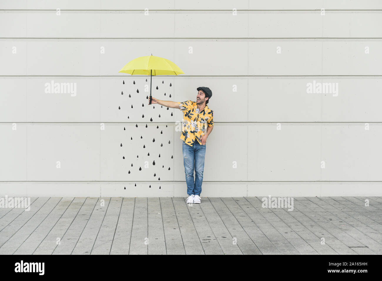 Digital composite of young man holding an umbrella at a wall with raindrops Stock Photo