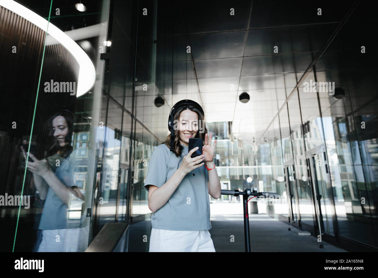 Woman with e-scooter and helmet using smartphone in a passage Stock Photo