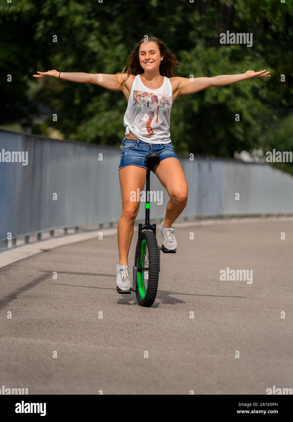 Smiling young woman riding unicycle on the street Stock Photo