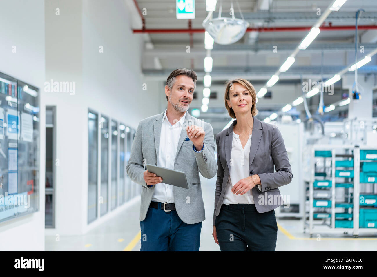 Businesswoman and businessman with tablet walking and talking in a modern factory Stock Photo
