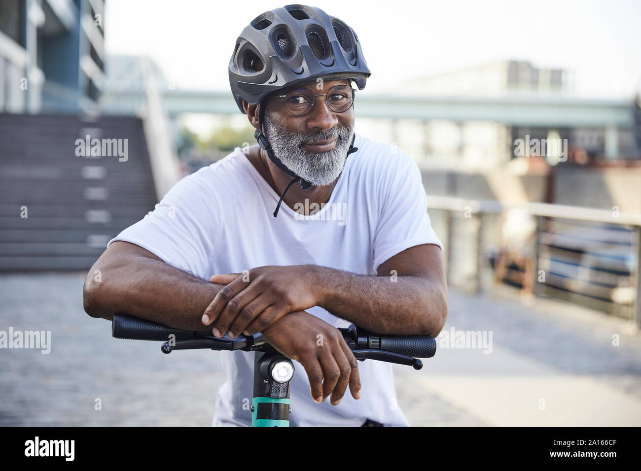 Portrait of smiling mature man wearing cycling helmet leaning on handlebar of Electric Scooter Stock Photo