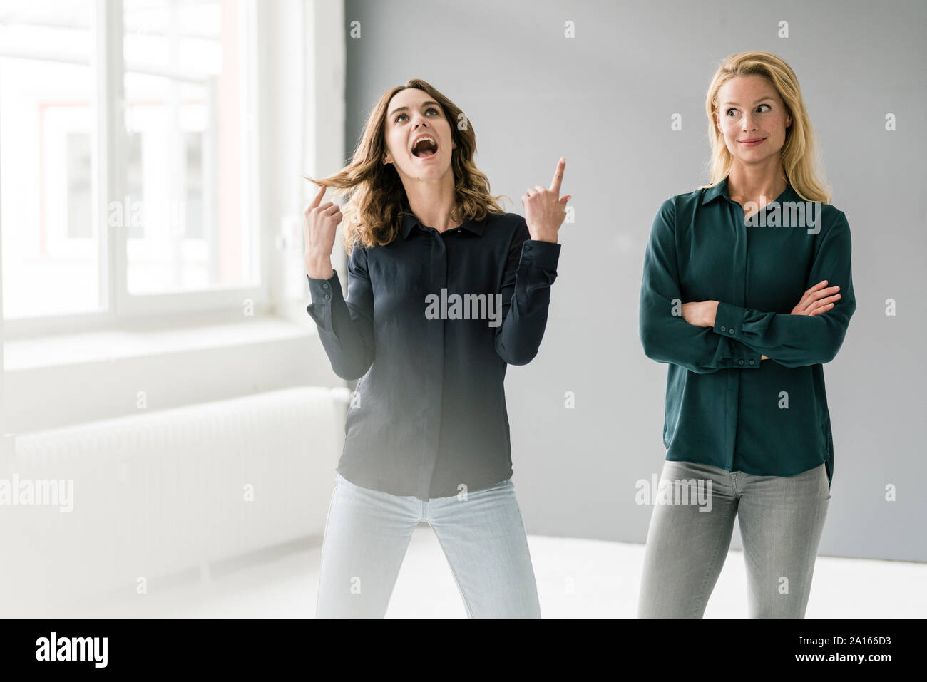 Two young businesswomen standing in bright room, imagining success Stock Photo