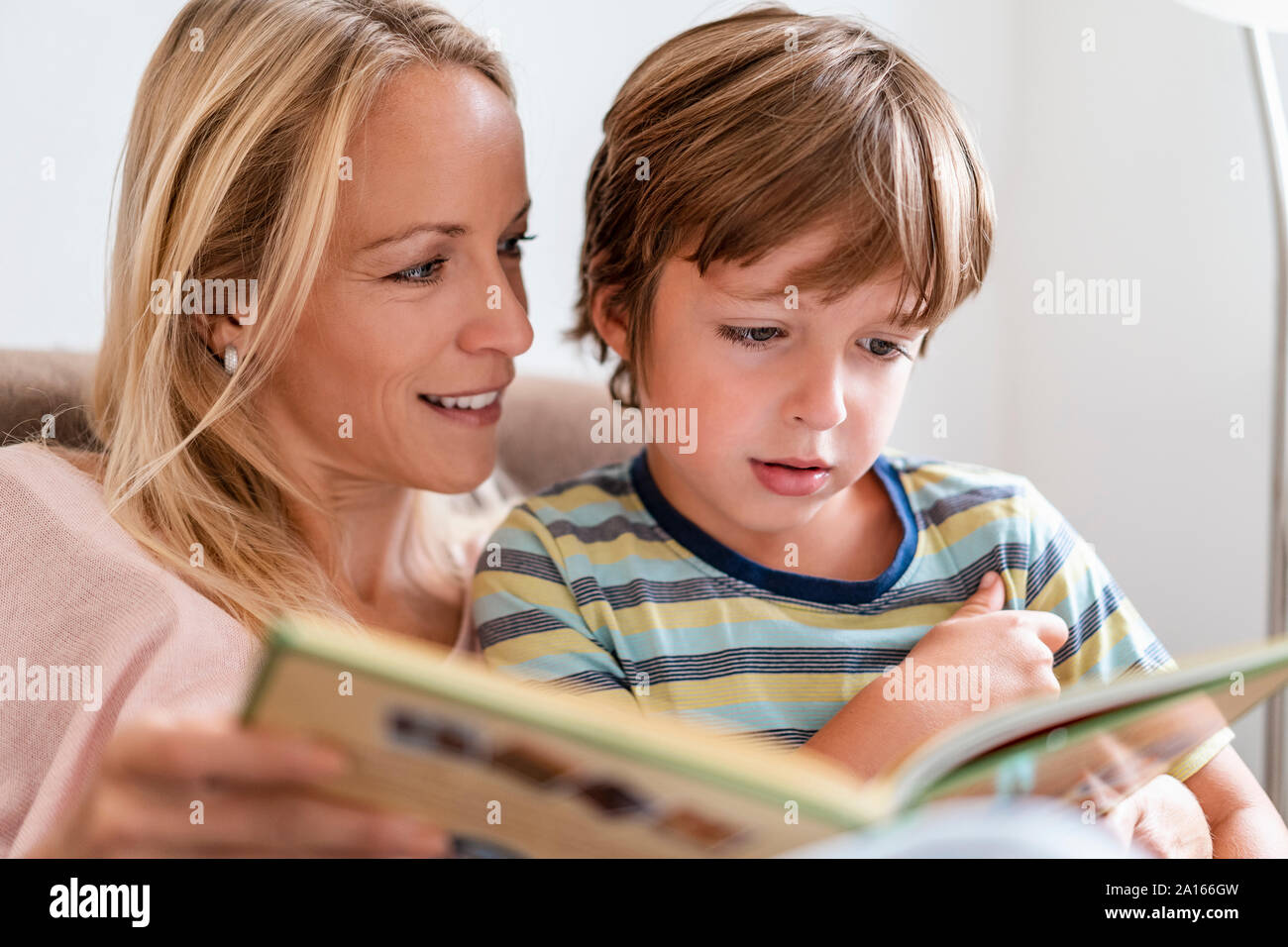 Mother and son reading a book together on couch at home Stock Photo