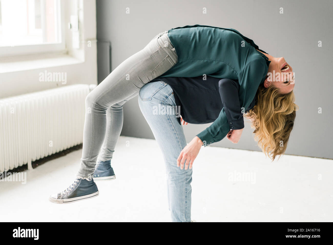 Two young women supporting each other playfully Stock Photo
