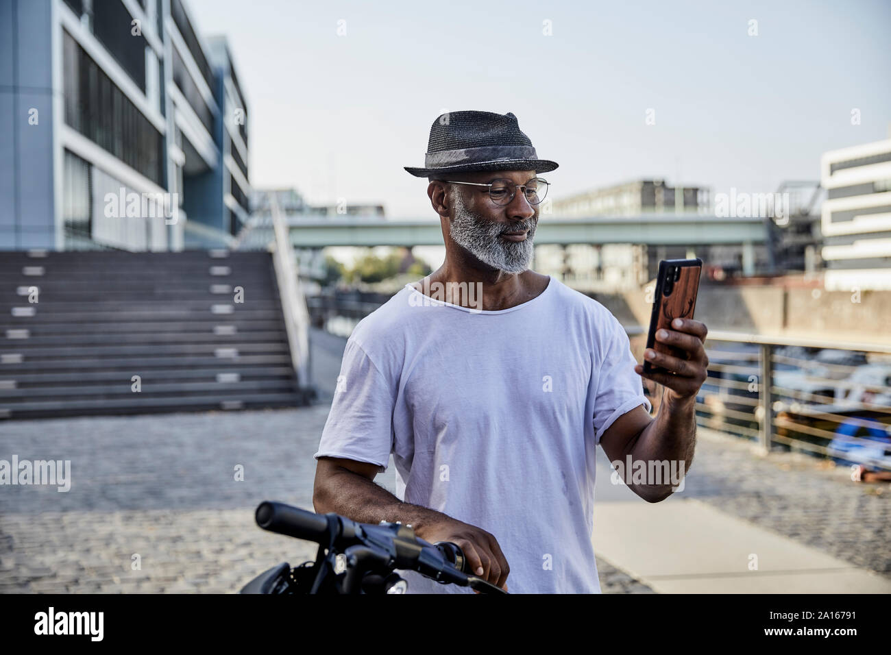 Portrait of smiling mature man with E-Scooter looking at mobile phone Stock Photo