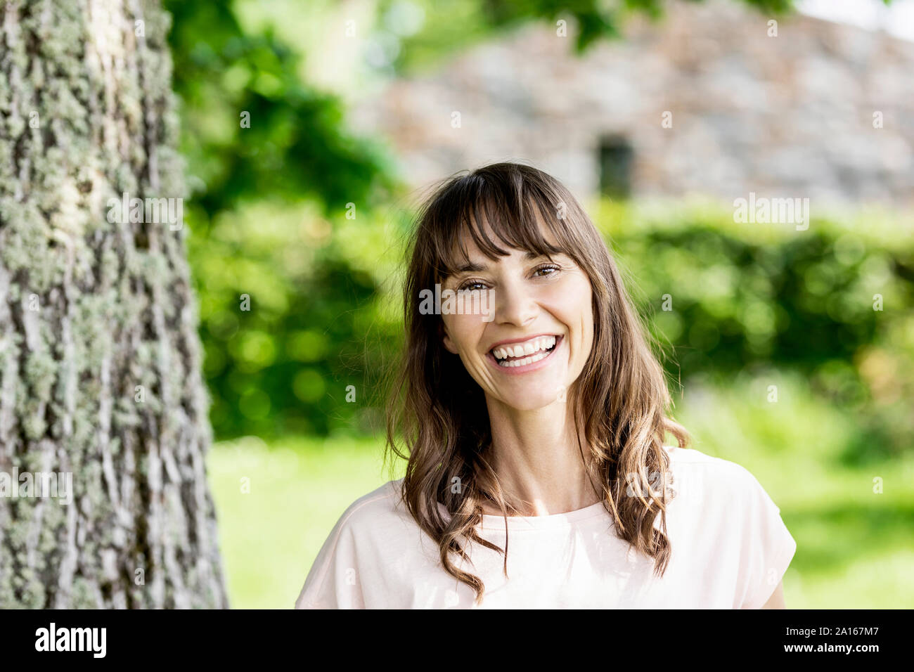 Portrait of happy brunette woman at a tree trunk Stock Photo