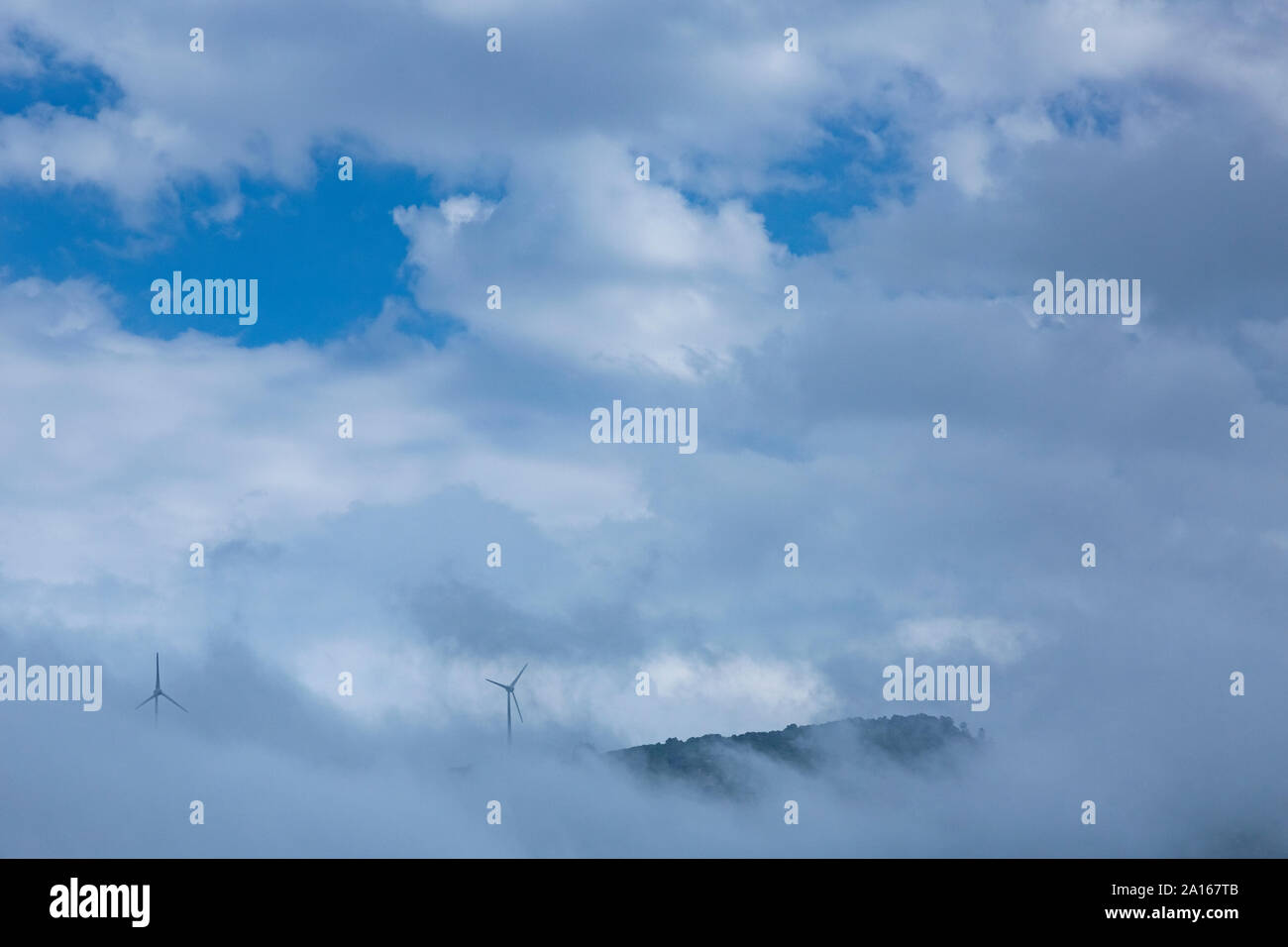 Wind turbines on mountain amidst clouds against sky Stock Photo