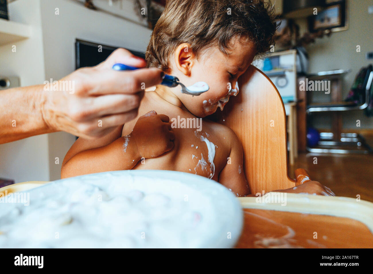 Little boy eating yogurt at home, turning away his head Stock Photo