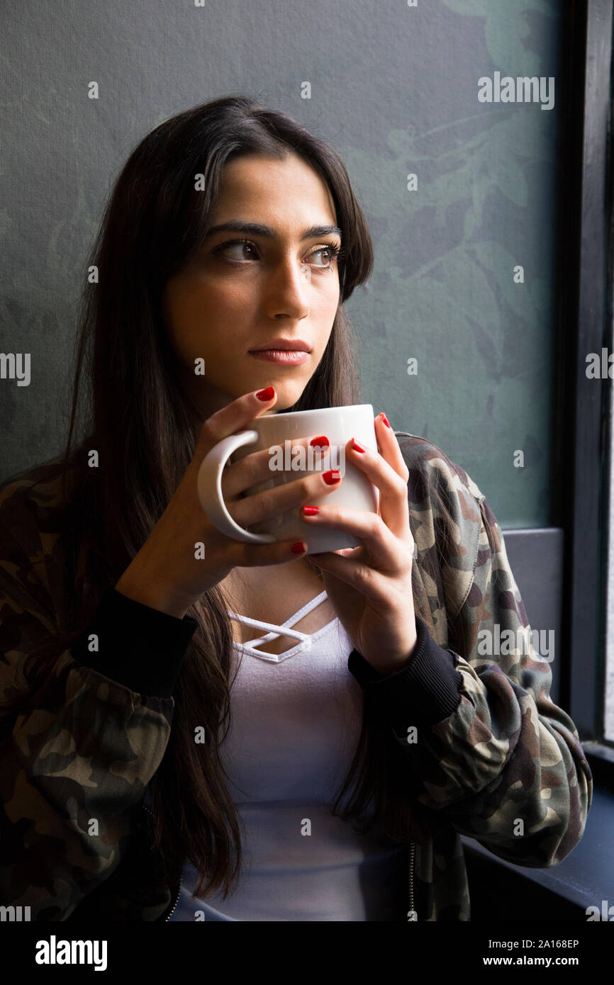 Young woman sitting in cafe with cup of coffee and looking sideways Stock Photo
