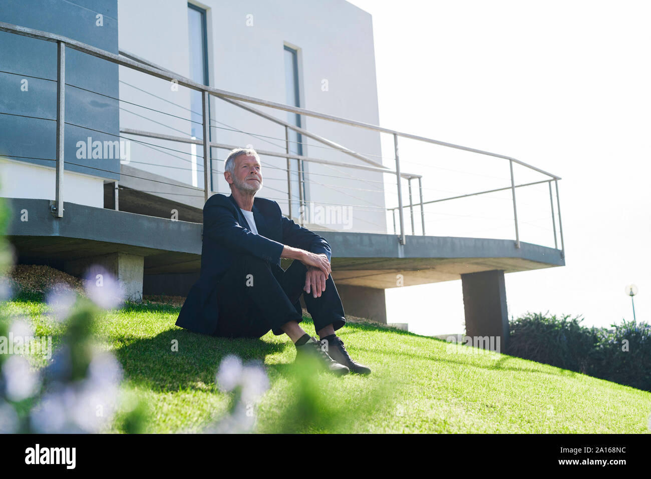 Senior businessman sitting on lawn outside a building Stock Photo