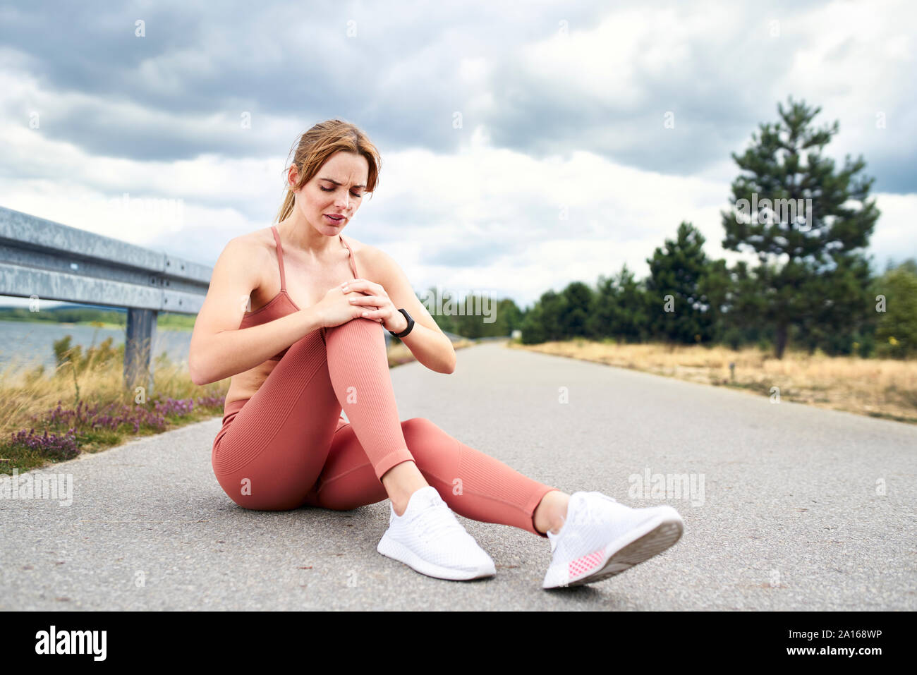 Woman sitting on ground and holding knee after injury during workout Stock Photo