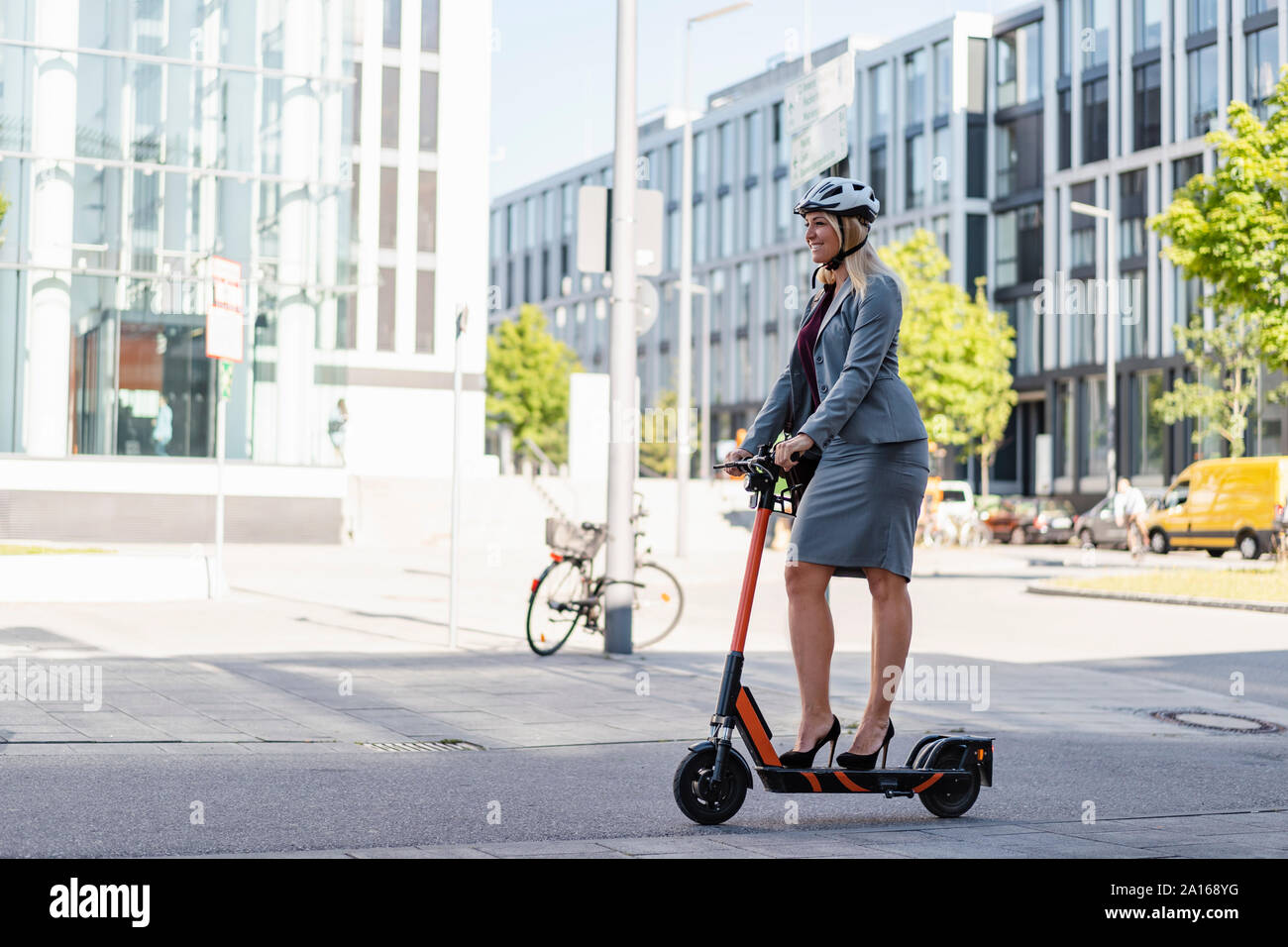 Smiling businesswoman wearing high heels riding electric scooter on the street Stock Photo