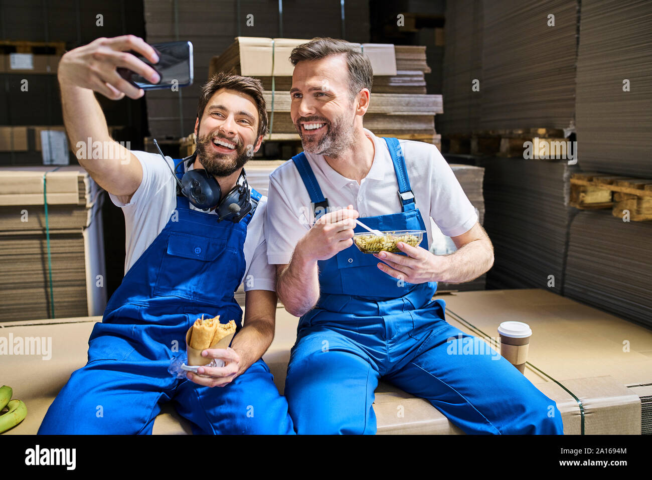 Two happy workers having lunch break and taking a selfie in factory Stock Photo