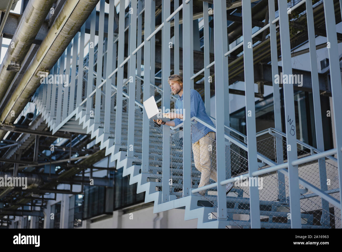 Young man standing on stairs using laptop Stock Photo