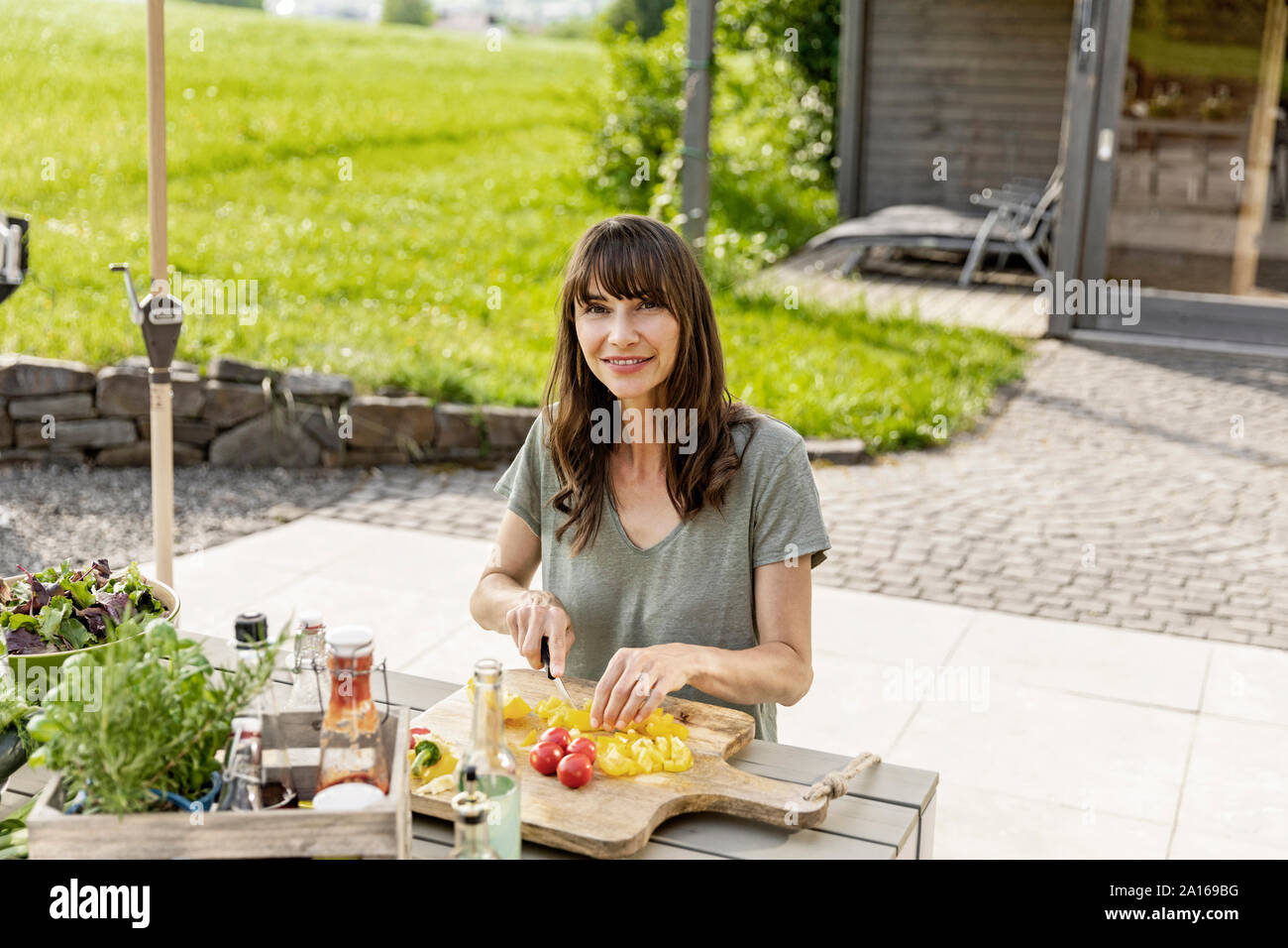 Portrait of smiling woman preparing a salad on garden table Stock Photo