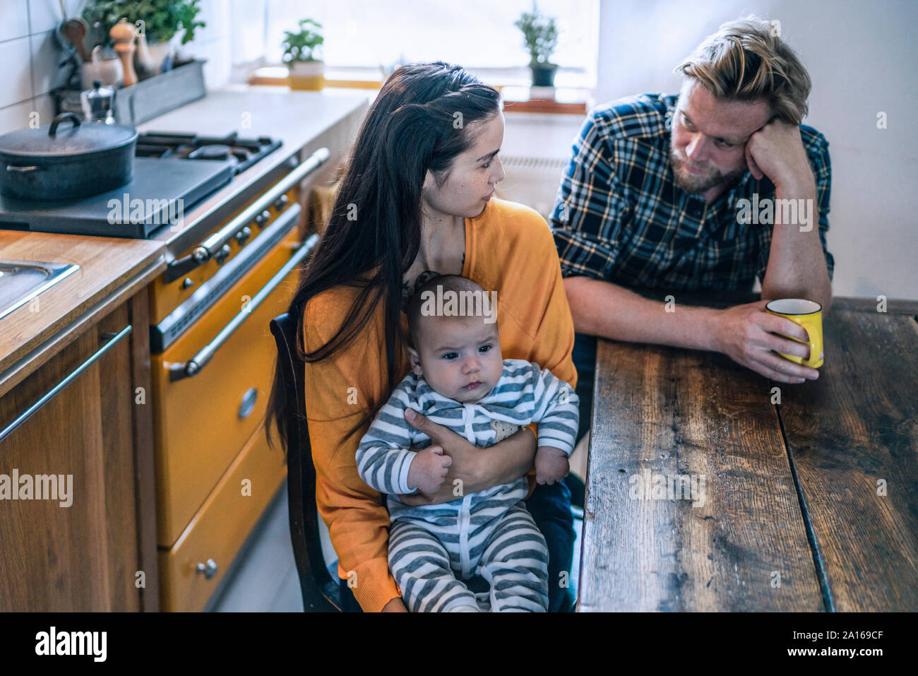 Serious family with baby sitting at kitchen table at home Stock Photo