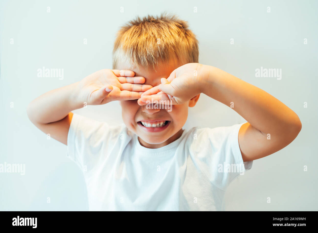 Boy covering his eyes in front of white background Stock Photo - Alamy