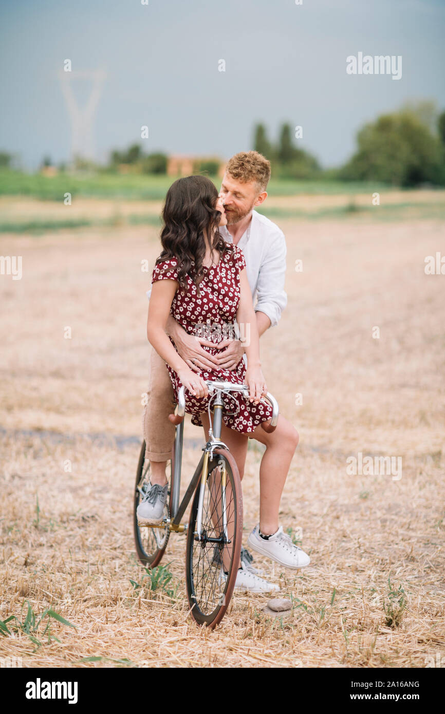 Kissing couple with handcrafted racing cycle on stubble field Stock Photo