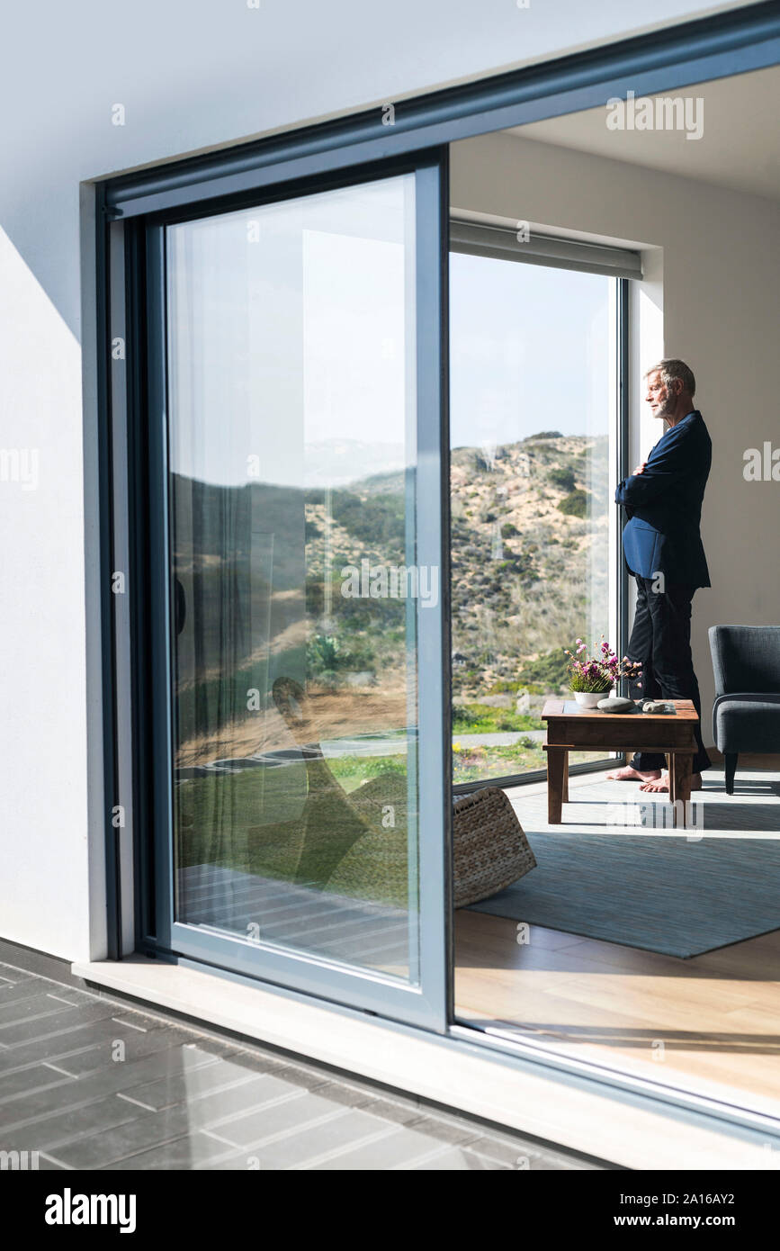 Senior businessman standing at panorama window looking out Stock Photo
