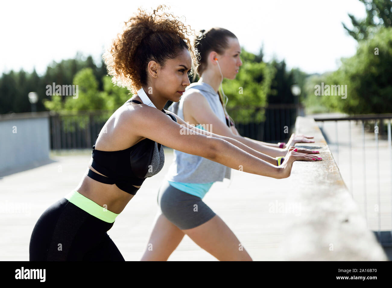 Two sporty young women stretching on bridge railing Stock Photo