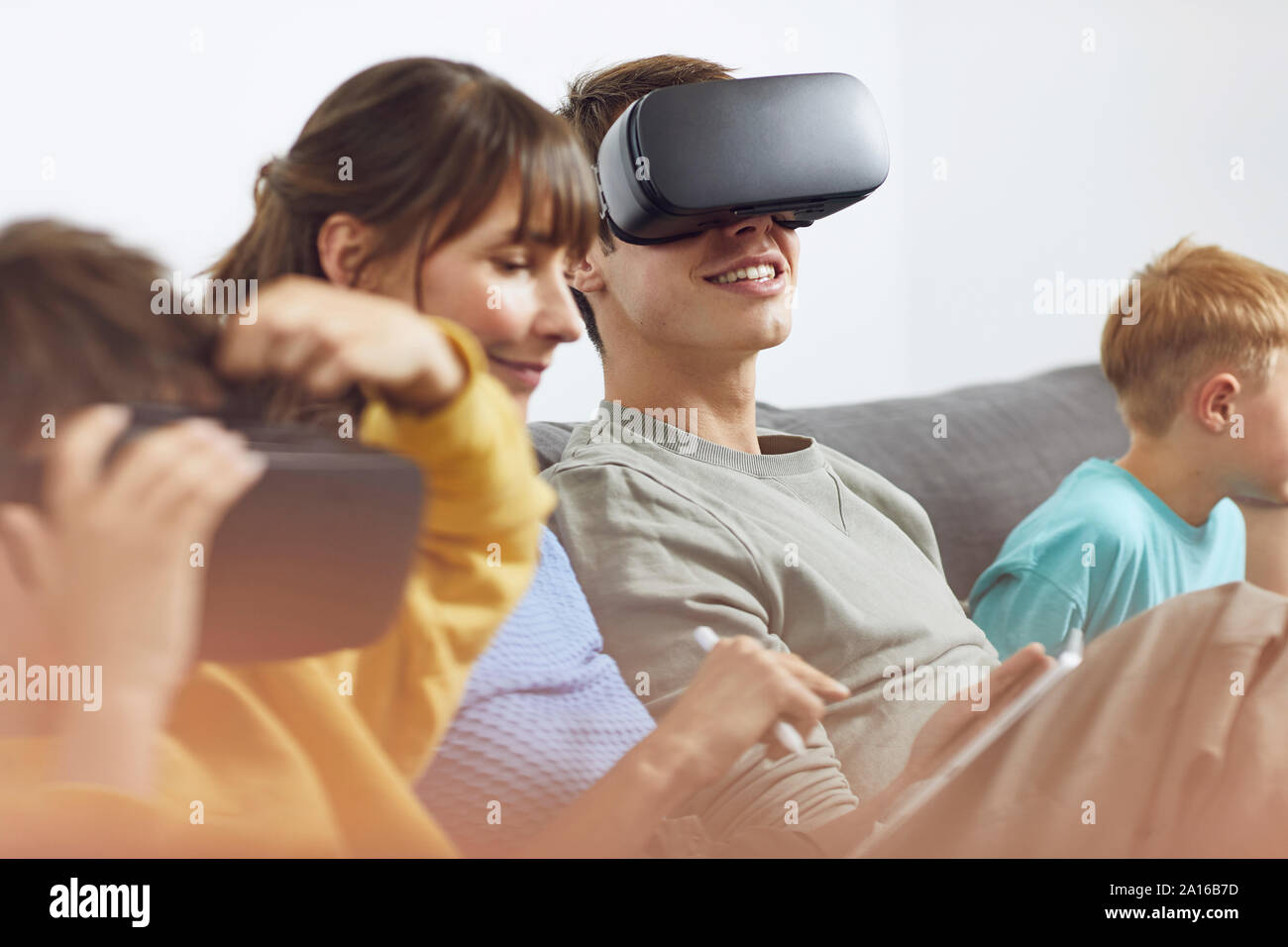 Happy family sitting on couch, using VR goggles and mobile devices