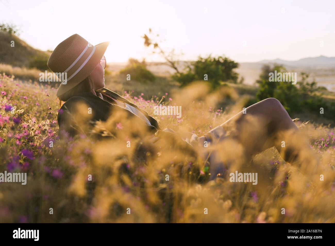 Young woman sitting on meadow at sunset Stock Photo