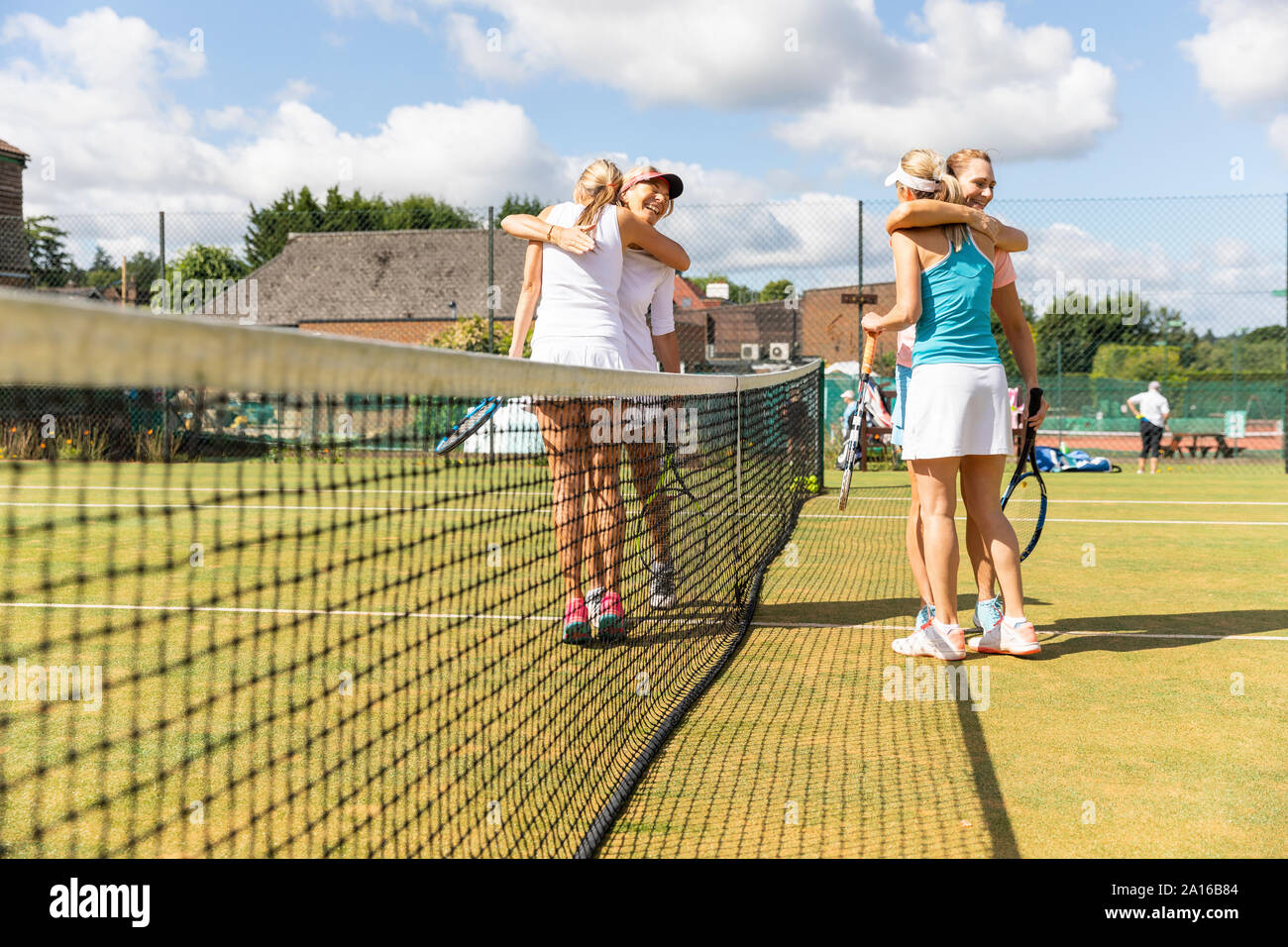 Mature women finishing tennis match on grass court hugging Stock Photo