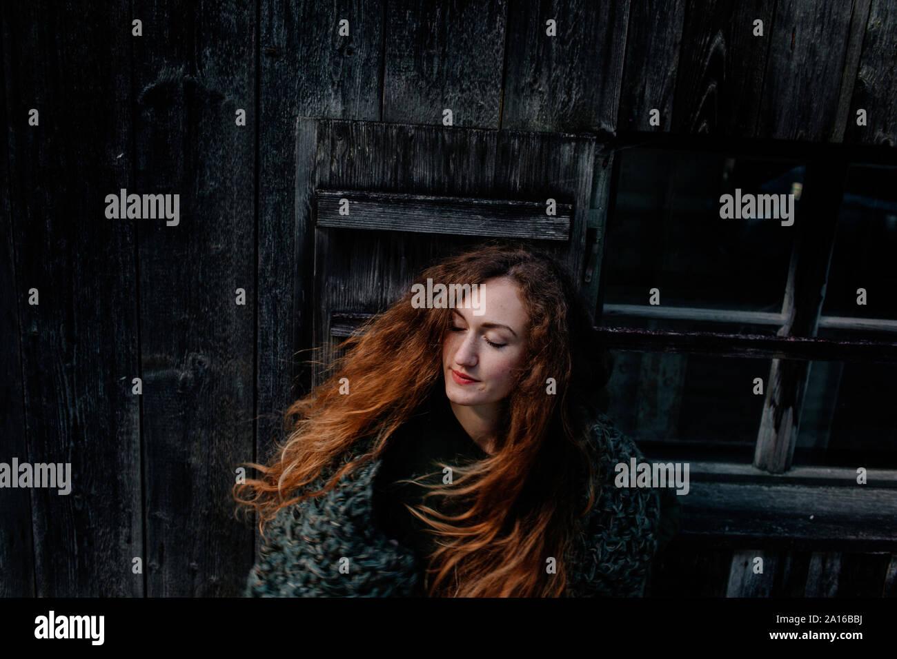 Portrait of redheaded woman with closed eyes, wooden wall in the background Stock Photo