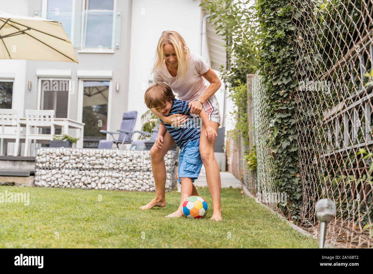 Happy mother and son playing football in garden Stock Photo