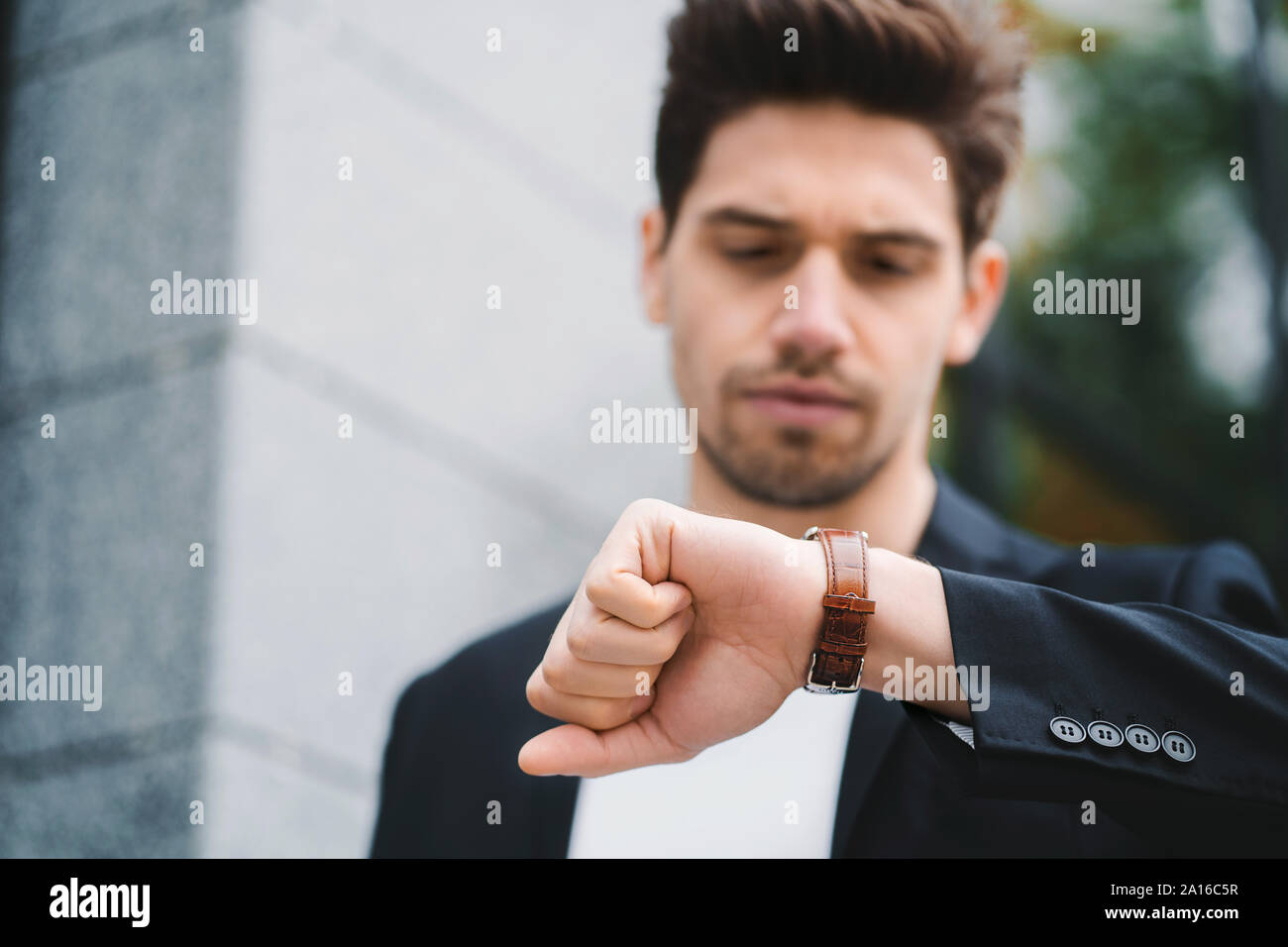 Handsome businessman or student looks at watch. Young man in hurry late for work. Male model on office building background Stock Photo