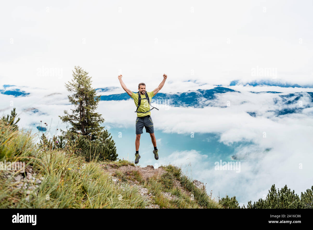 Happy young man with raised arms on a hiking trip in the mountains, Herzogstand, Bavaria, Germany Stock Photo