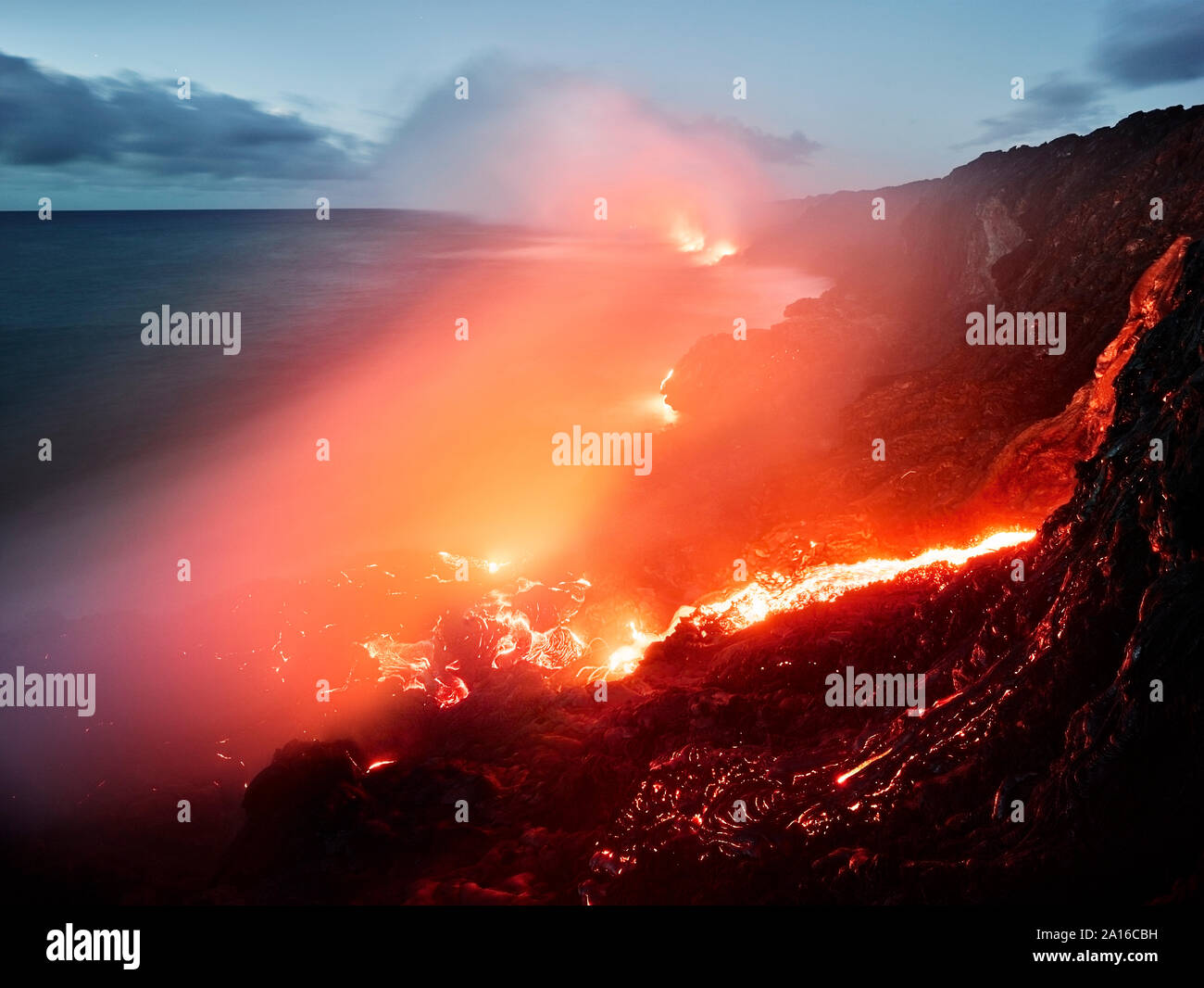 Glowing orange lava flowing from Pu'u O'o' in sea at Hawaii Volcanoes National Park against sky Stock Photo