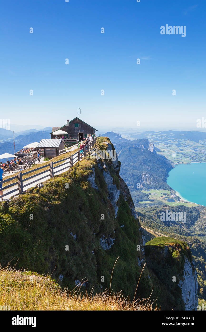 Tourists at Himmelspforte Schafberg on mountain peak with lake on sunny day Stock Photo