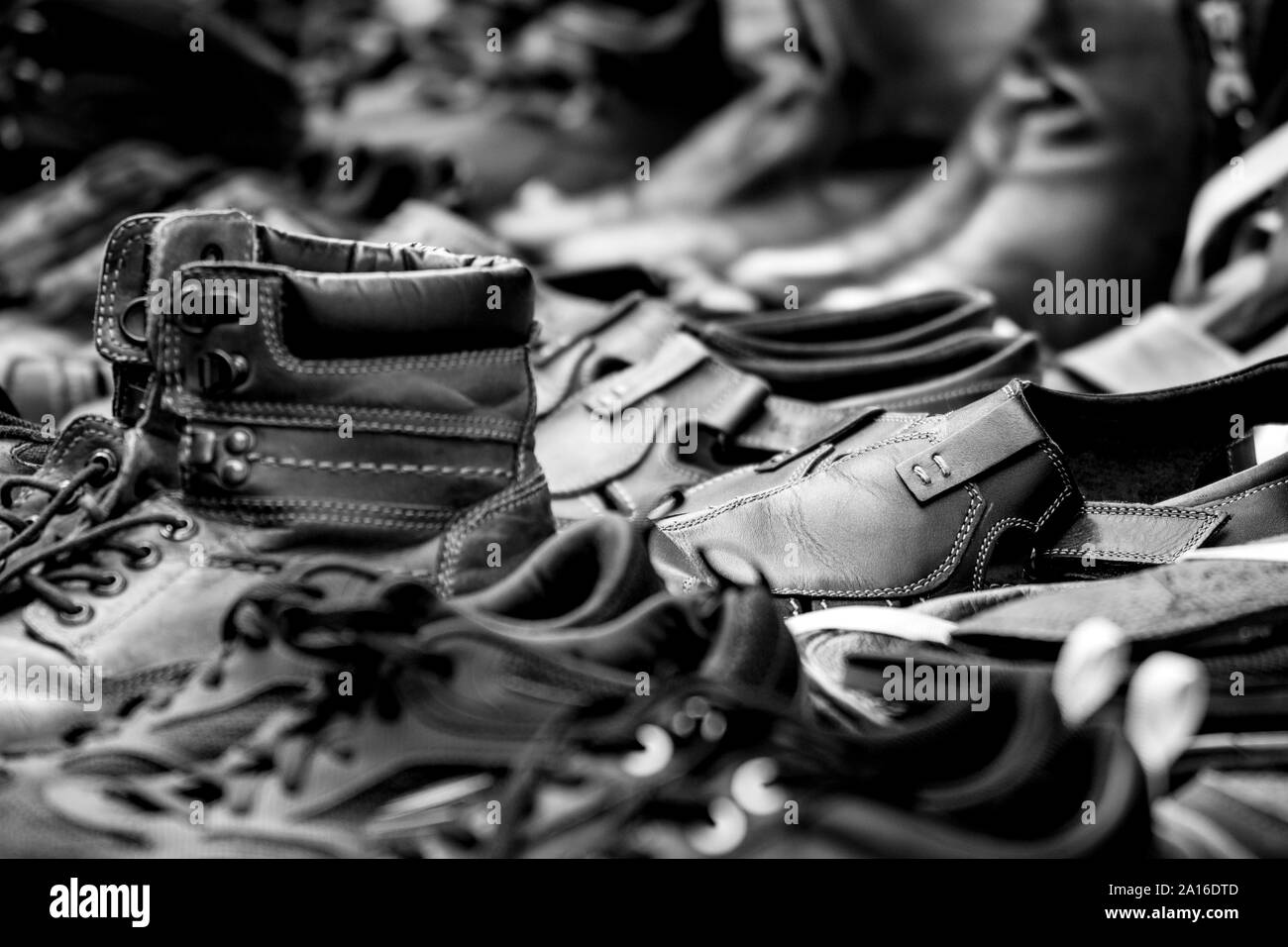 A black and white photo of a collection of aligned pairs of  worn shoes; blurred  front and background. Stock Photo