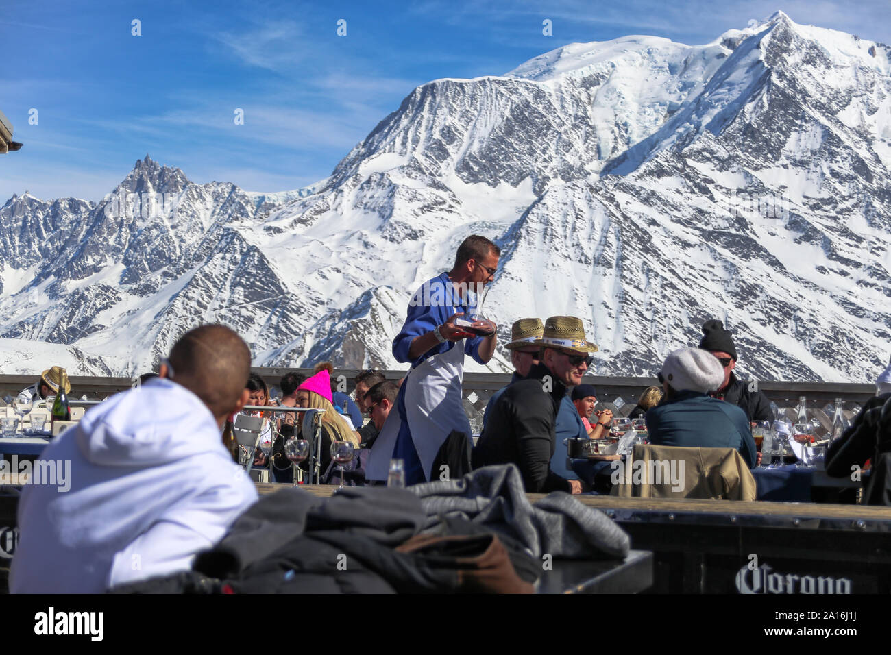 Wine waiter serves customers with wine decanter. Mont Blanc in the back on a sunny day. La Folie Douce Saint Gervais apres ski restaurant of Chamonix. Stock Photo