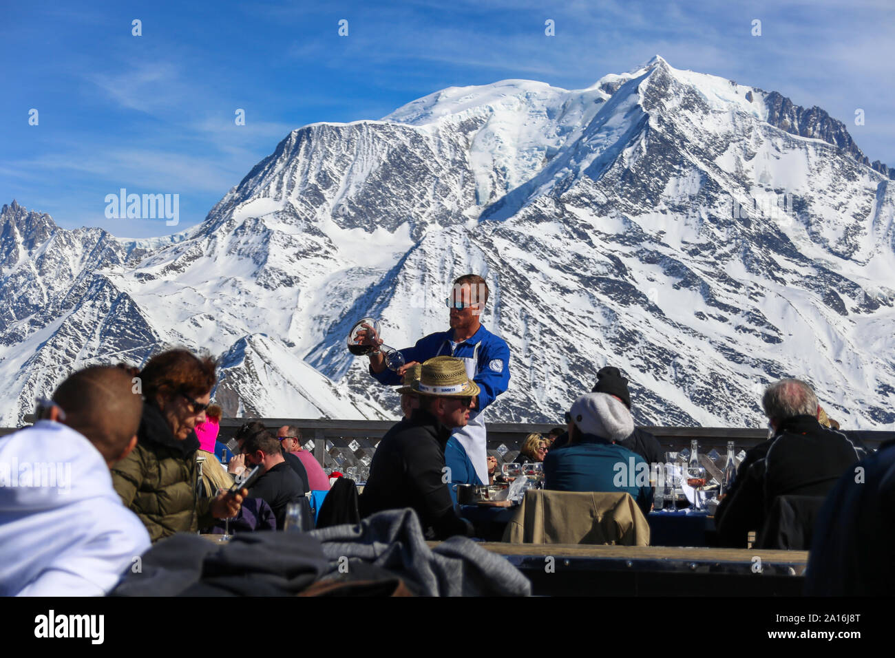 Wine waiter serves customers with wine decanter. Mont Blanc in the back on a sunny day. La Folie Douce Saint Gervais After Ski  Restaurantof Chamonix. Stock Photo
