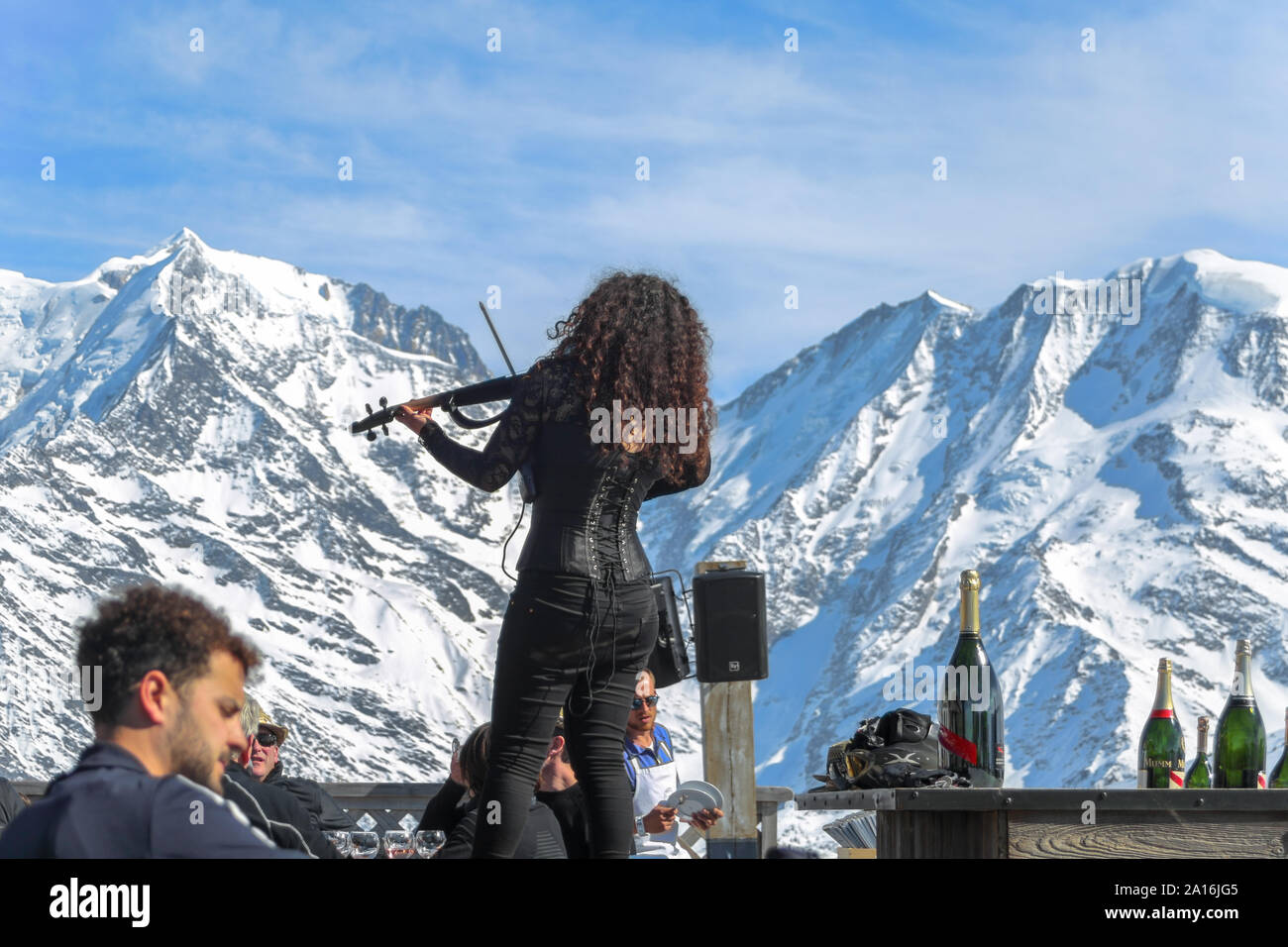 Woman plays violin in an outdoor ski restaurant. Snow covered Mont Blanc in the back on a sunny winter day. La Folie Douce Saint Gervais of Chamonix. Stock Photo