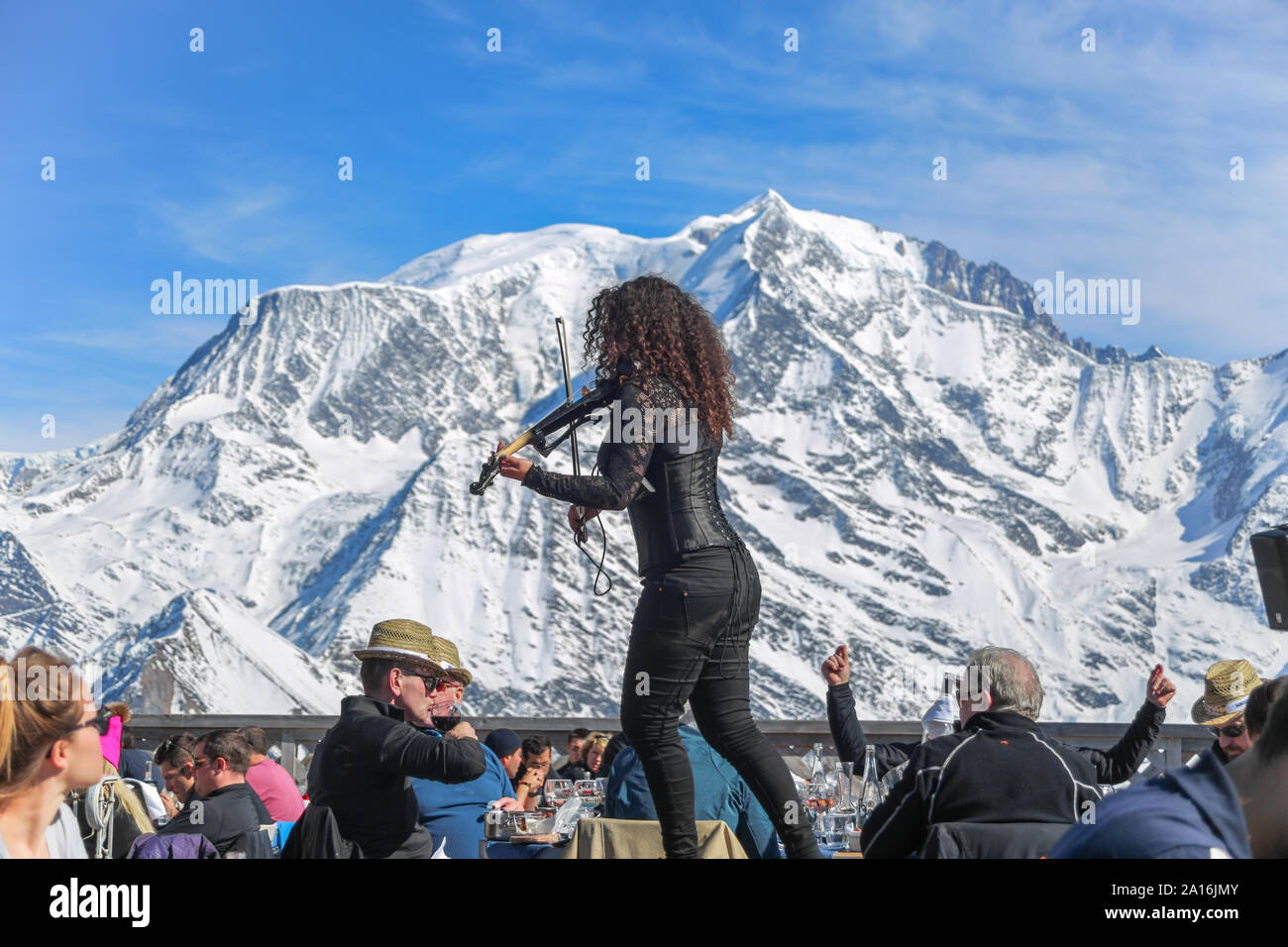 Woman playing violin at after ski restaurant. Mont Blanc in the back on a sunny winter day. La Folie Douce Saint Gervais Restaurant of Chamonix. Stock Photo