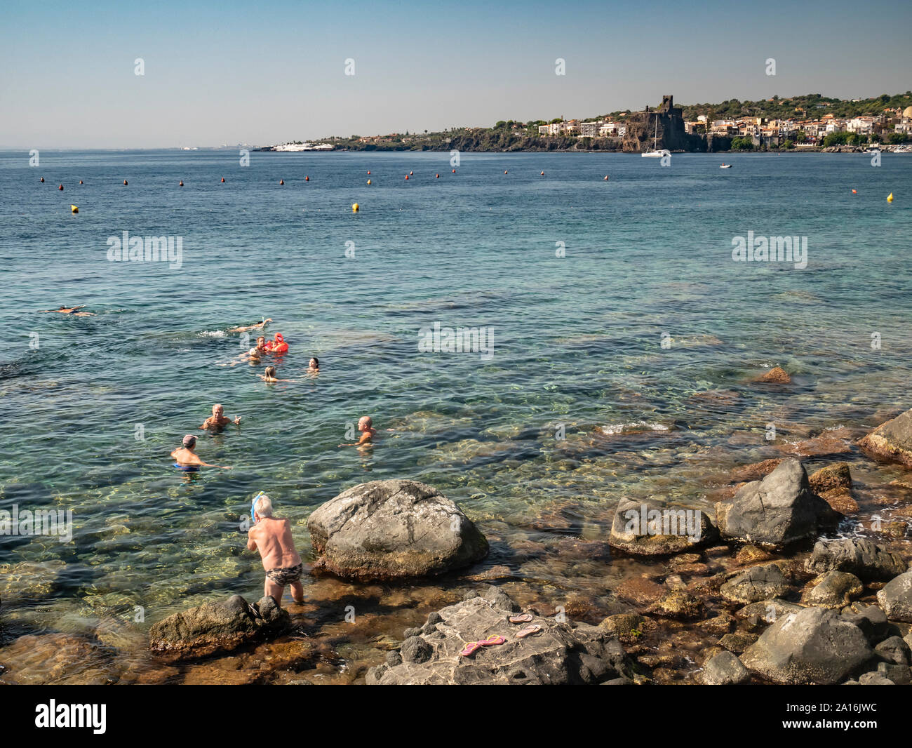Bathers at Acitrezza in Sicily with the castle of Acicastello in the background Stock Photo