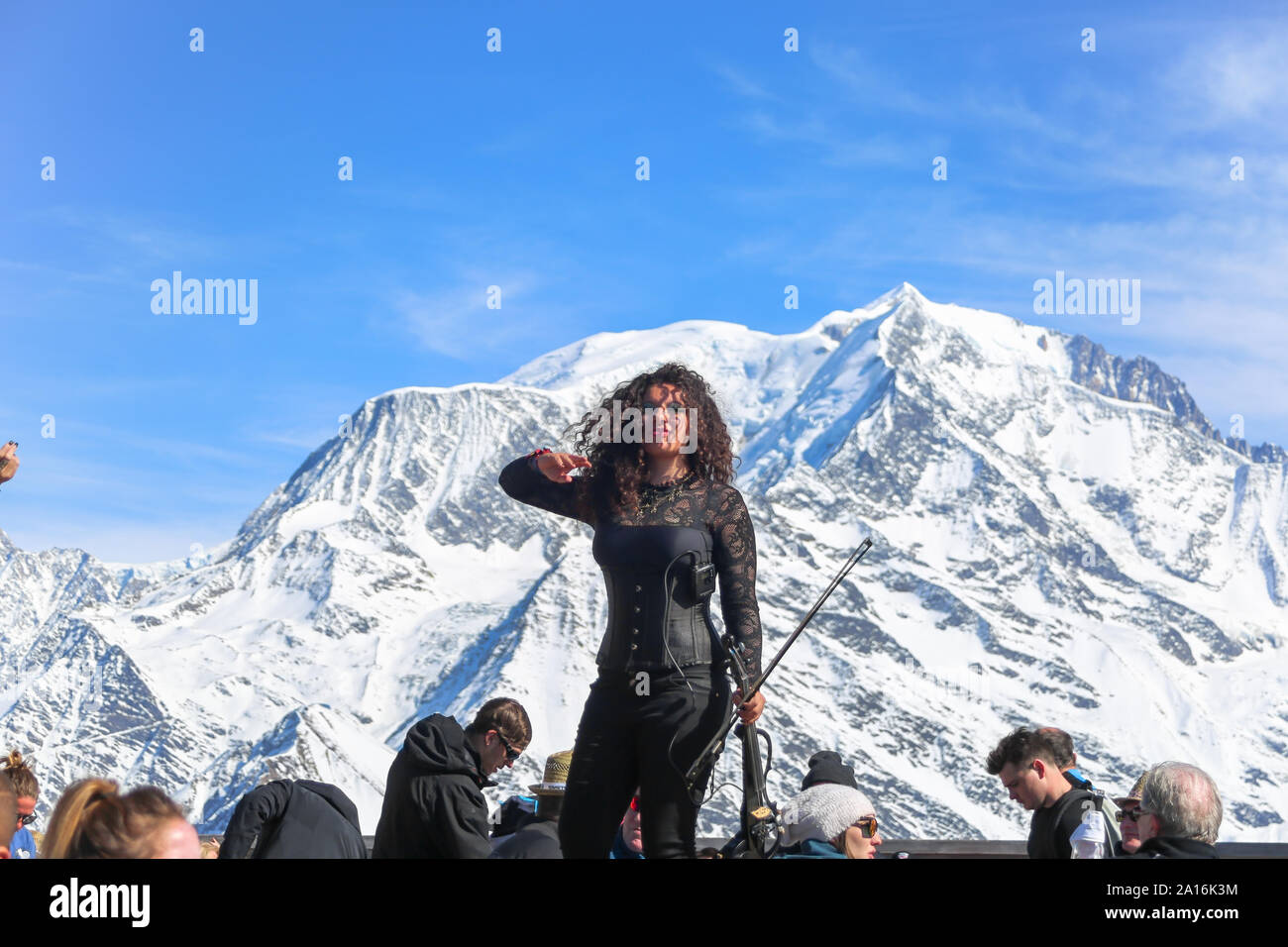 Violinist woman greets audience. Snow capped Mont Blanc in the background on a sunny winter day. La Folie Douce Saint Gervais Restaurant of Chamonix. Stock Photo