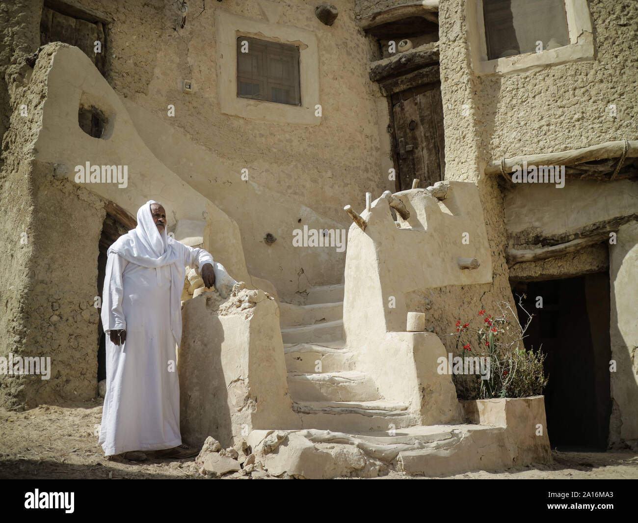 A Siwi Berber Amazigh man stands ahead of a Siwan traditional house made of "Kharsif". Stock Photo