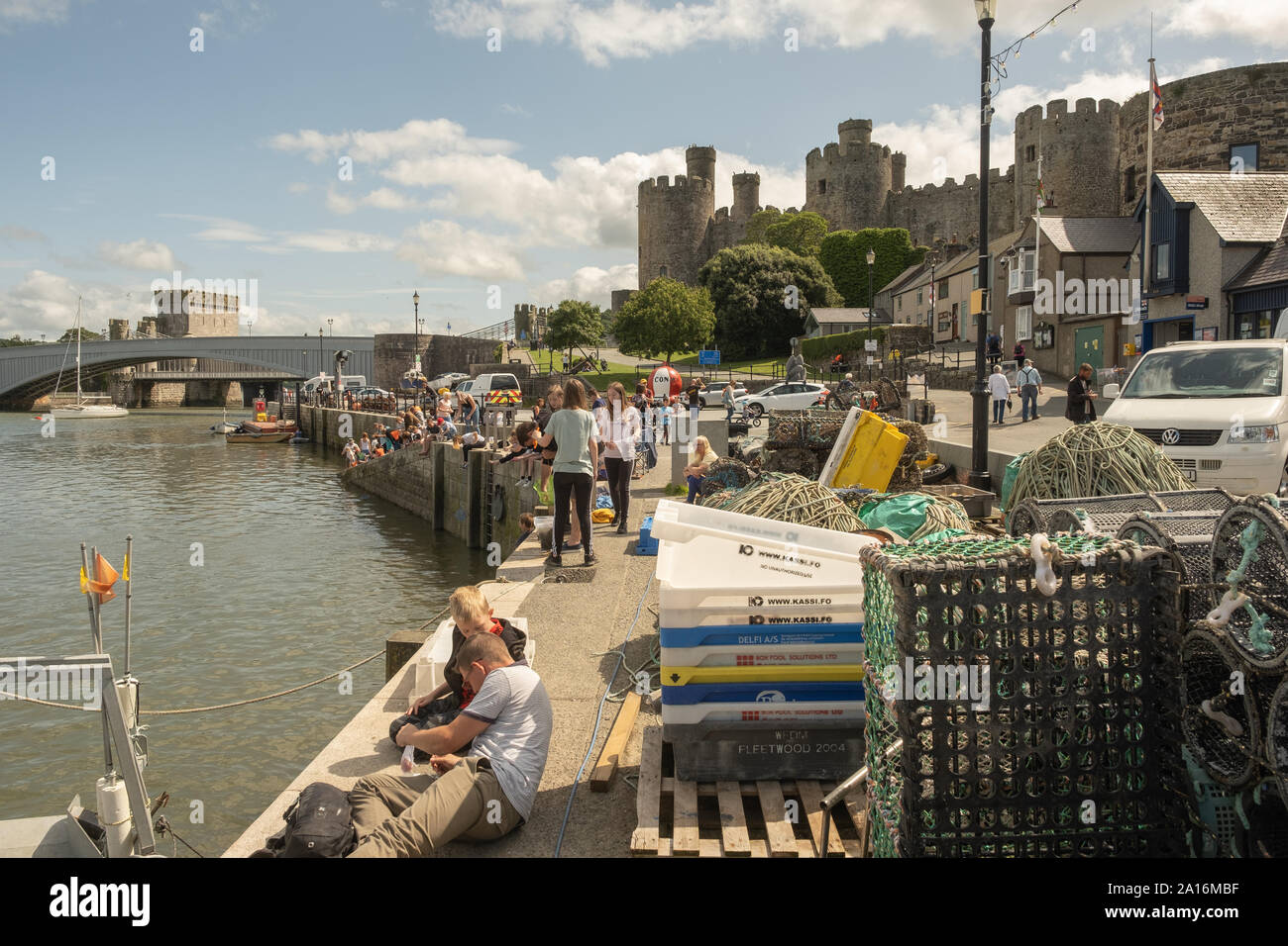 Tourists enjoying a warm and sunny summer afternoon on the quayside in the shadow of the historic castle and town  of Conwy, [Conway] Gwynedd, north Wales UK Stock Photo