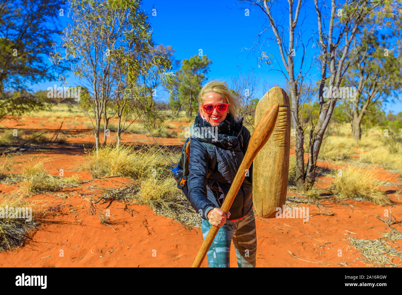 Happy tourist woman holding an aboriginal weapon of spear and a wooden shield used by Luritja and Pertame people, Central Australia, Northern Stock Photo