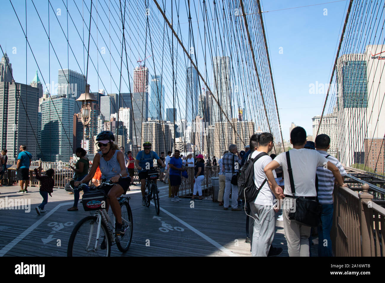 Fußgänger und Fahradfahrer teilen sich die obere Etage der Brooklyn Bridge. Touristen genießen den Blick auf Manhattan Stock Photo